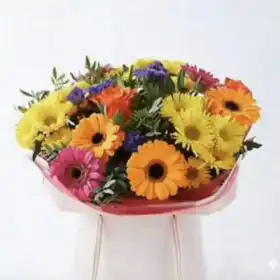 A hand-tied orange and yellow gerbera bouquet accented with roses and lush greenery in a bright setting.