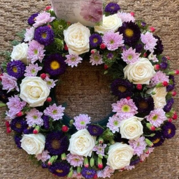 A beautiful Purple and White Funeral Wreath composed of fresh cream roses and vibrant violet blossoms.