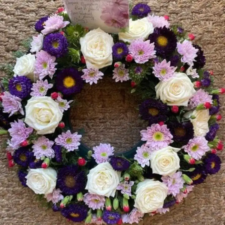 Elegant Purple and White Funeral Wreath 1 A beautiful Purple and White Funeral Wreath composed of fresh cream roses and vibrant violet blossoms.