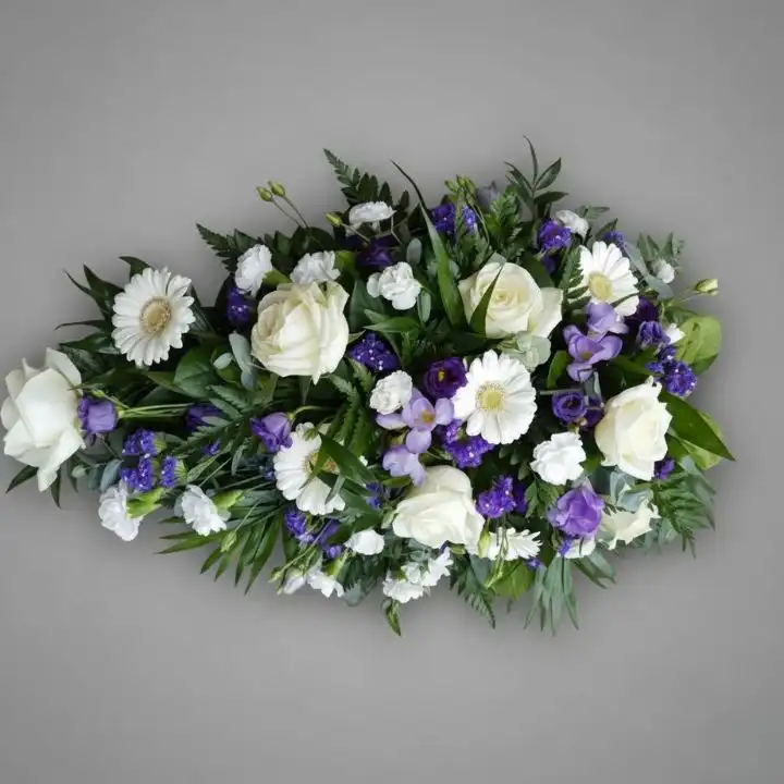 Funeral Flowers Coffin Sprays 1 A casket topped with a serene arrangement of purple and white funeral flowers coffin sprays featuring lilies and roses.