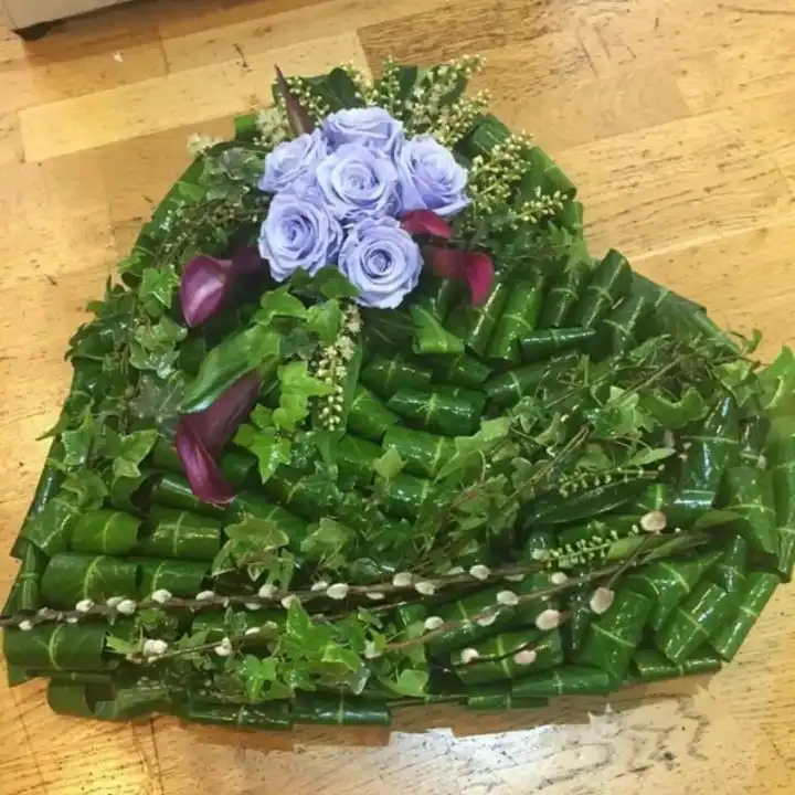 Large Heart Funeral Tribute 1 Handcrafted Large Heart Funeral Tribute featuring lavender roses and deep purple calla lilies on a green leaf base.