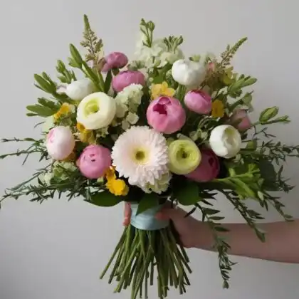 A lush ranunculus and peony bouquet featuring soft pink and white petals arranged with green foliage.