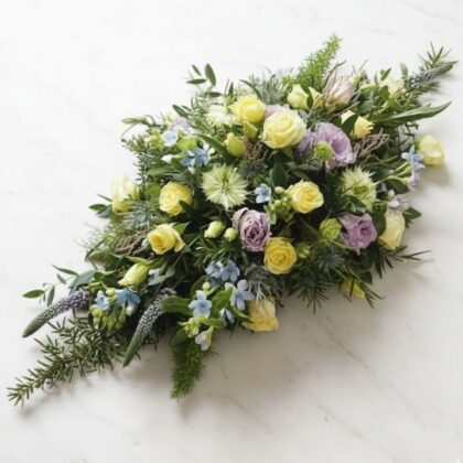 Beautiful Small Coffin Spray featuring yellow roses, lilac lisianthus, and mixed seasonal greenery for a heartfelt funeral tribute.