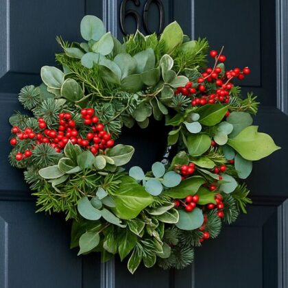 A traditional, beautifully crafted Christmas wreath with red berries and pinecones hanging on a wooden door, perfect for holiday decoration.