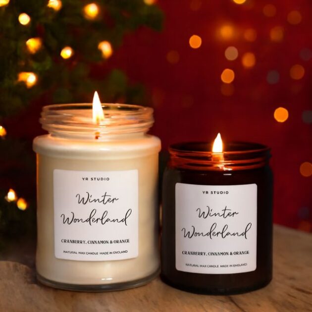 ( Candle Set ) Luxury Christmas scented 1 A set of two burning luxury Christmas scented candles in glass jars, scented with Cranberry, Cinnamon & Orange, set against holiday lights.
