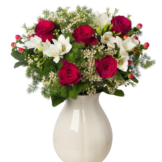 A festive Christmas flower vase arrangements featuring red roses, white freesia, hypericum berries, and fern in a white ceramic vase. Christmas floral vases for sales