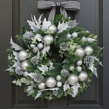 An elegant and contemporary Silver and White Christmas wreath decorated with glittery ornaments, metallic ribbon, and frosted leaves, hanging on a minimalist door.