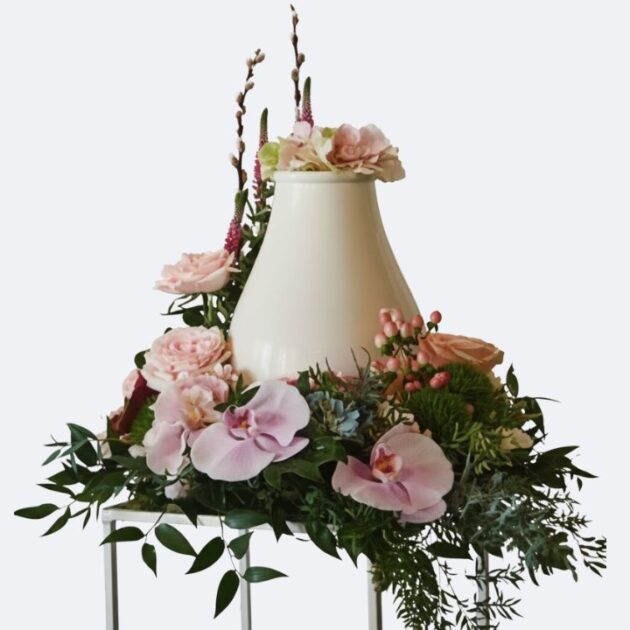 Funeral Urn Flower Arrangements featuring soft pink orchids, roses, and lush greenery for a respectful memorial display.