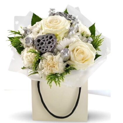 Festive white rose and carnation flower bouquet gift bag with silver accents, dried lotus pods, and holiday foliage, ready for presentation. Buy White Christmas Flower Bouquet arrangements For next day delivery