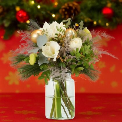 A festive Christmas flower vase arrangement with white blooms, pine needles, dried grass, and gold ornaments in a clear jar vase. Christmas Vase Flowers for sale