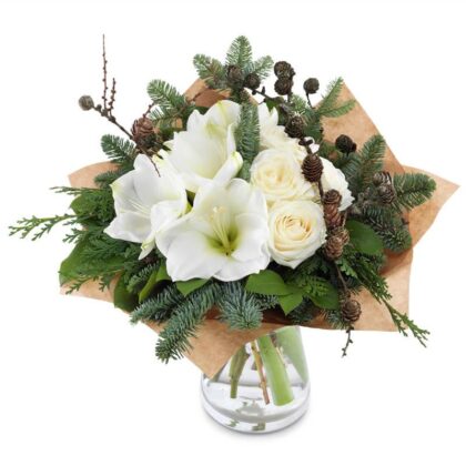A beautiful, unique Christmas flower arrangements featuring white amaryllis and roses with pine branches and cones, wrapped in brown paper and set in a vase. Buy Amaryllis Flowers For Christmas
