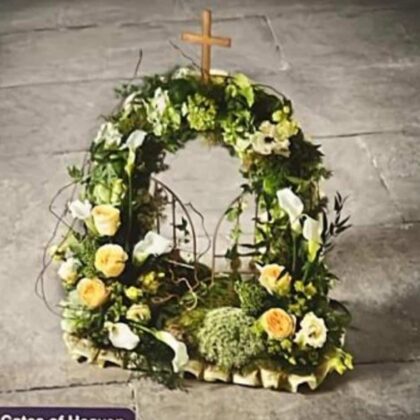 Gates of Heaven floral tribute with a cross, white lilies, and yellow roses.