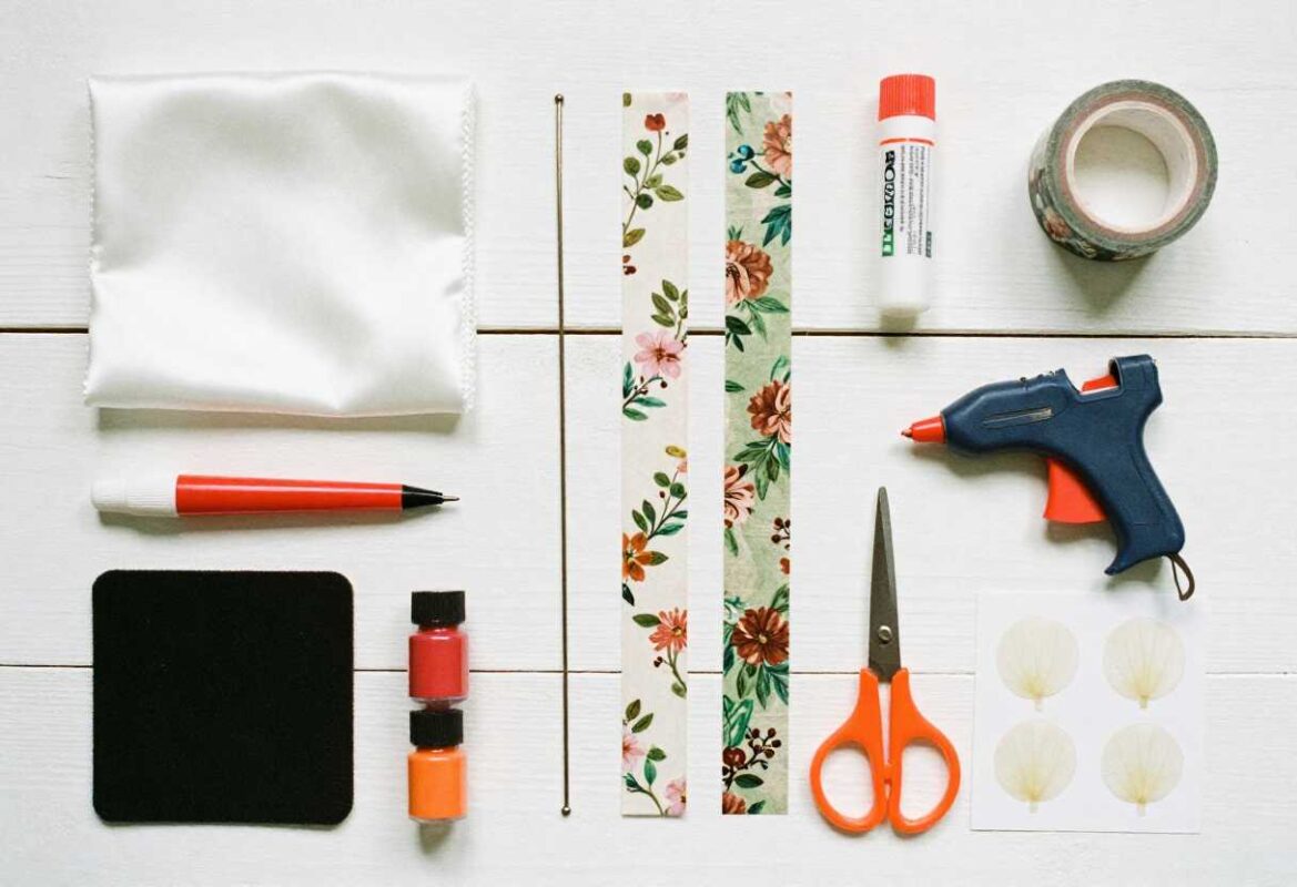 Flat lay of artificial flower making supplies including fabric, wire, floral tape, scissors, and crafting tools
